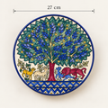 A round ceramic wall plaque featuring a hand-painted tree of life design with blue and green leaves, a red trunk, and various animals under the tree. The plaque is shown against a plain off-white background with a dimension line indicating a width of 27 cm.